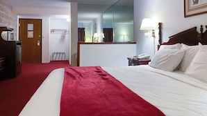 A hotel room with a bed, a red throw, a telephone, a mirror, and a door. - Voyageur Inn and Conference Center (Reedsburg)