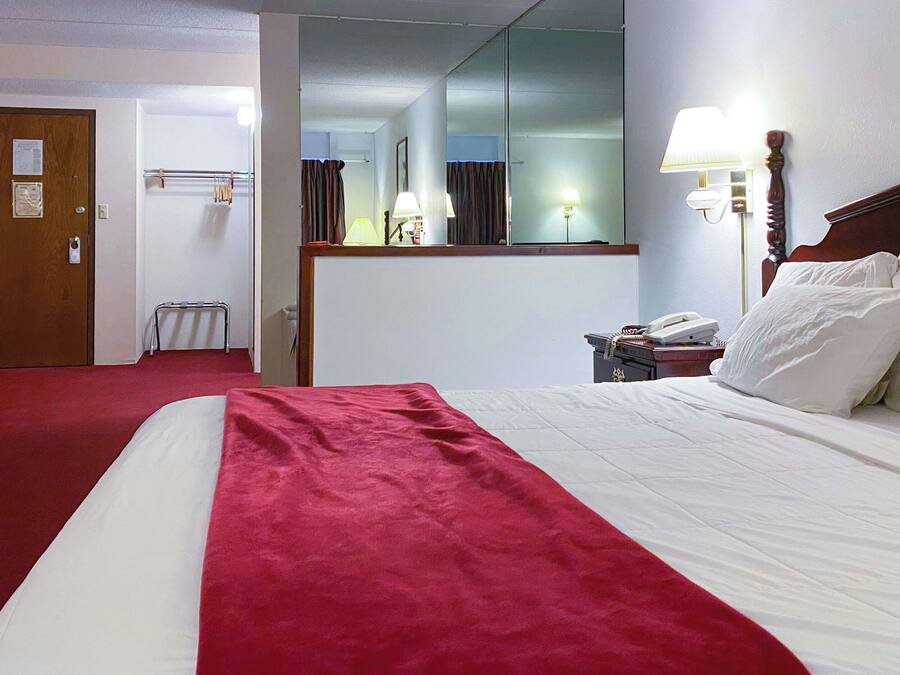 A hotel room with a bed, a red throw, a telephone, a mirror, and a door.