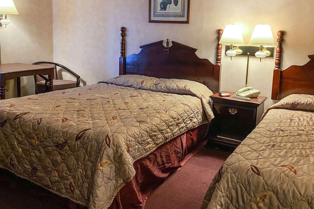 Habitación de hotel con dos camas, un escritorio y una mesita de noche con lámpara y teléfono.