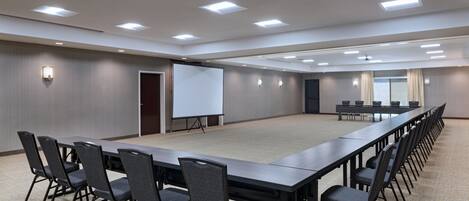 A conference room with a long table, chairs, a projector screen, and a carpeted floor.