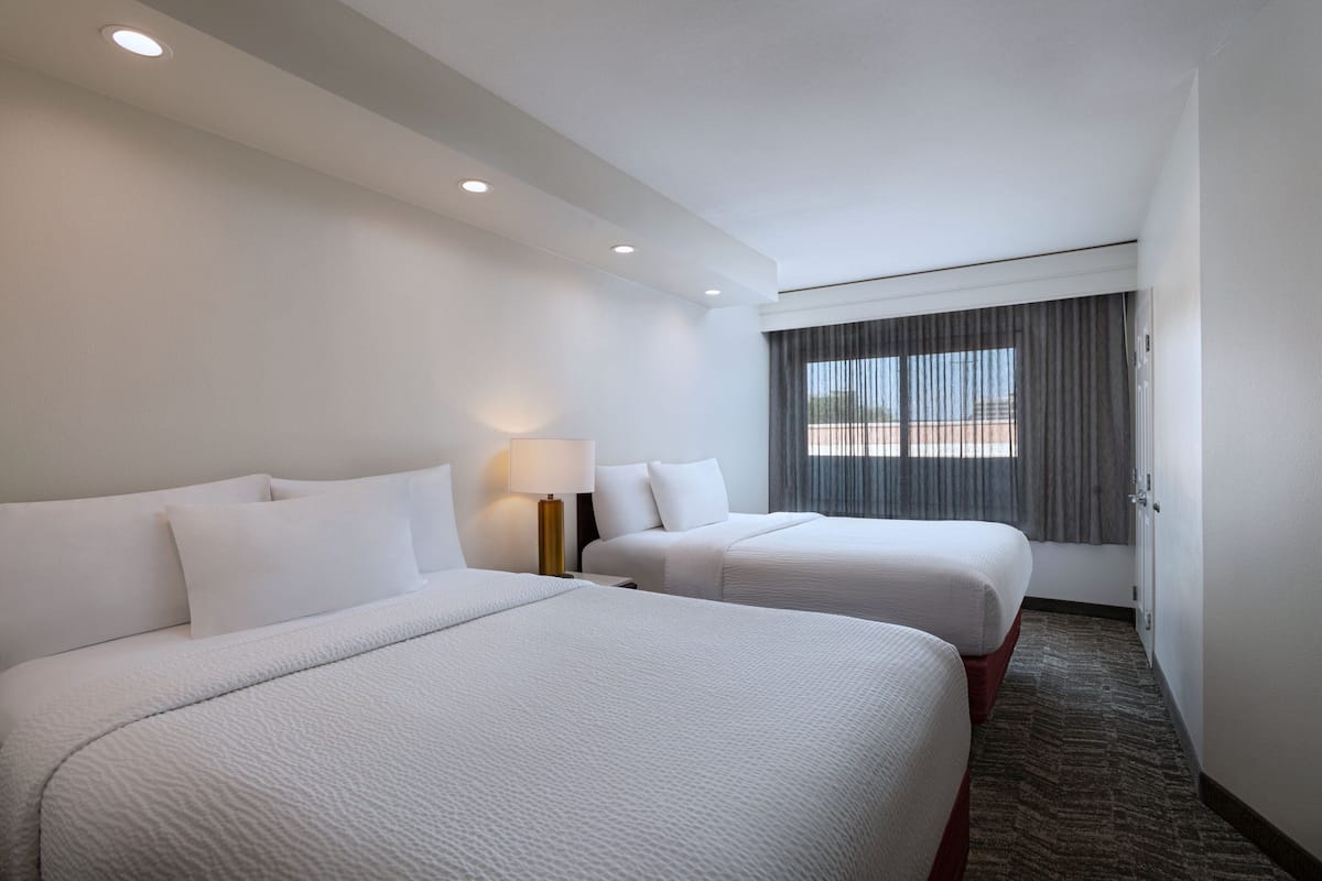 Habitación de hotel con dos camas, una ventana con cortinas y piso alfombrado.