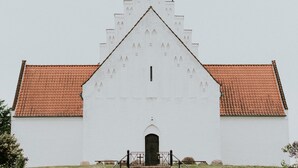 Un bâtiment blanc avec un toit recouvert de tuiles rouges, une entrée centrale et une façade symétrique.