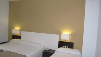Une chambre d’hôtel avec deux lits, chacun doté de draps blancs et d’une tête de lit sombre. Il y a deux tables de chevet, chacune avec une lampe et un téléphone. Les murs sont de couleur beige, et la chambre présente un design simple et épuré.