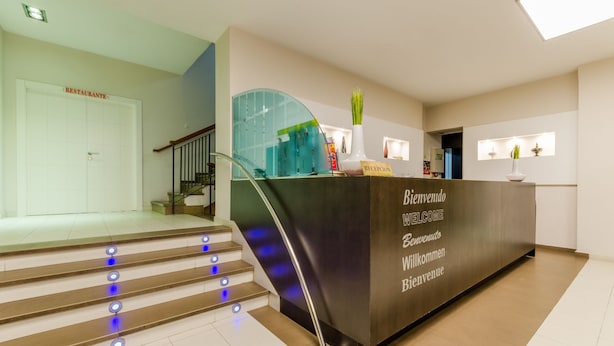 A reception desk with a sign that reads "Welcome" in multiple languages, a staircase with blue lights, and a door labeled "Restaurant". - Hotel Don Juan (Granada)