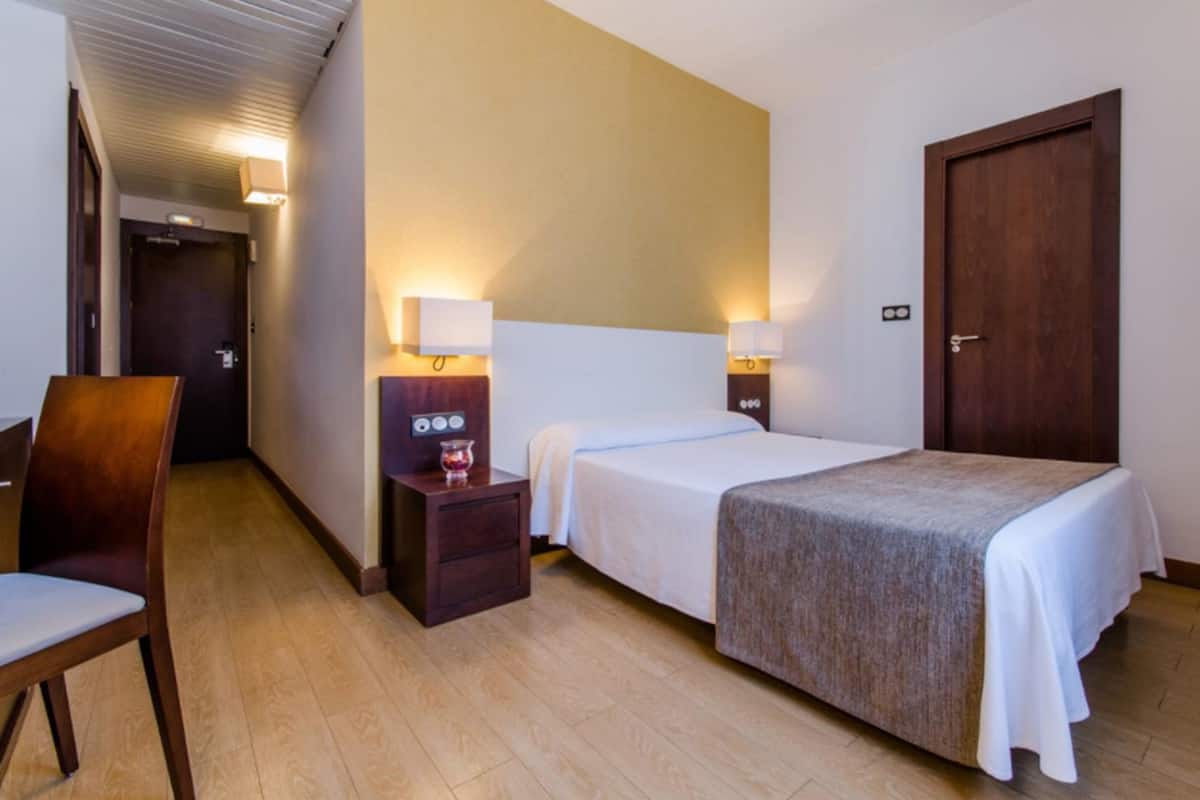 Una habitación de hotel con una cama, mesitas de noche, una silla y una puerta.