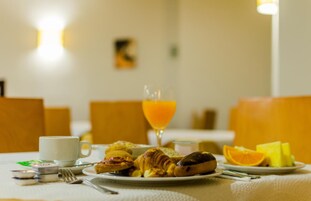 Desayuno con croissants, pasteles, un vaso de jugo de naranja y una fuente de fruta sobre una mesa.