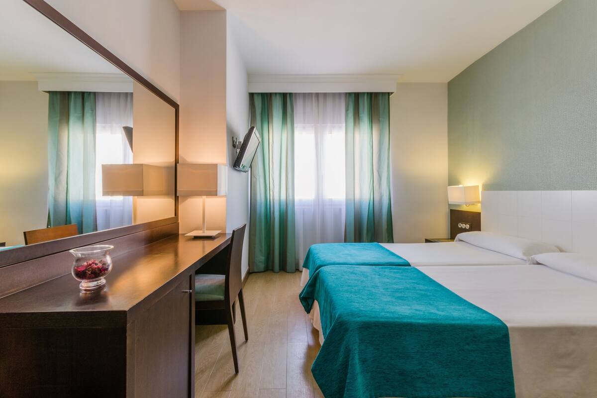 Habitación de hotel con cama, escritorio, silla, lámpara y espejo.