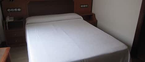 A single bed with a wooden headboard, two bedside lamps, and a nightstand with a phone.