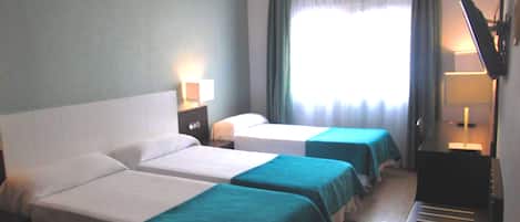Habitación de hotel con dos camas individuales, un escritorio con silla, televisor y ventana con cortinas.