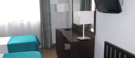 A hotel room with two beds, a desk, a chair, a TV, and a window with curtains.