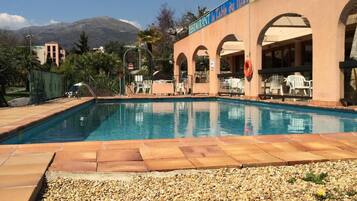 A swimming pool with a pebble border, a restaurant named "La Table du Mas," and a mountainous backdrop.