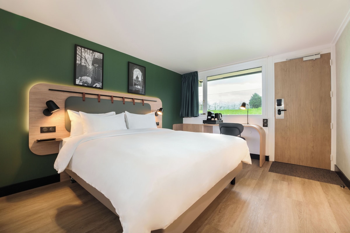 A hotel room with a large bed, a desk, and a window with a view of the outdoors.