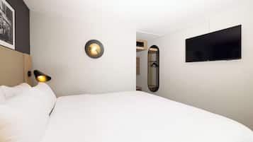 A hotel room with a bed, a wall-mounted TV, a bedside lamp, and a mirror.