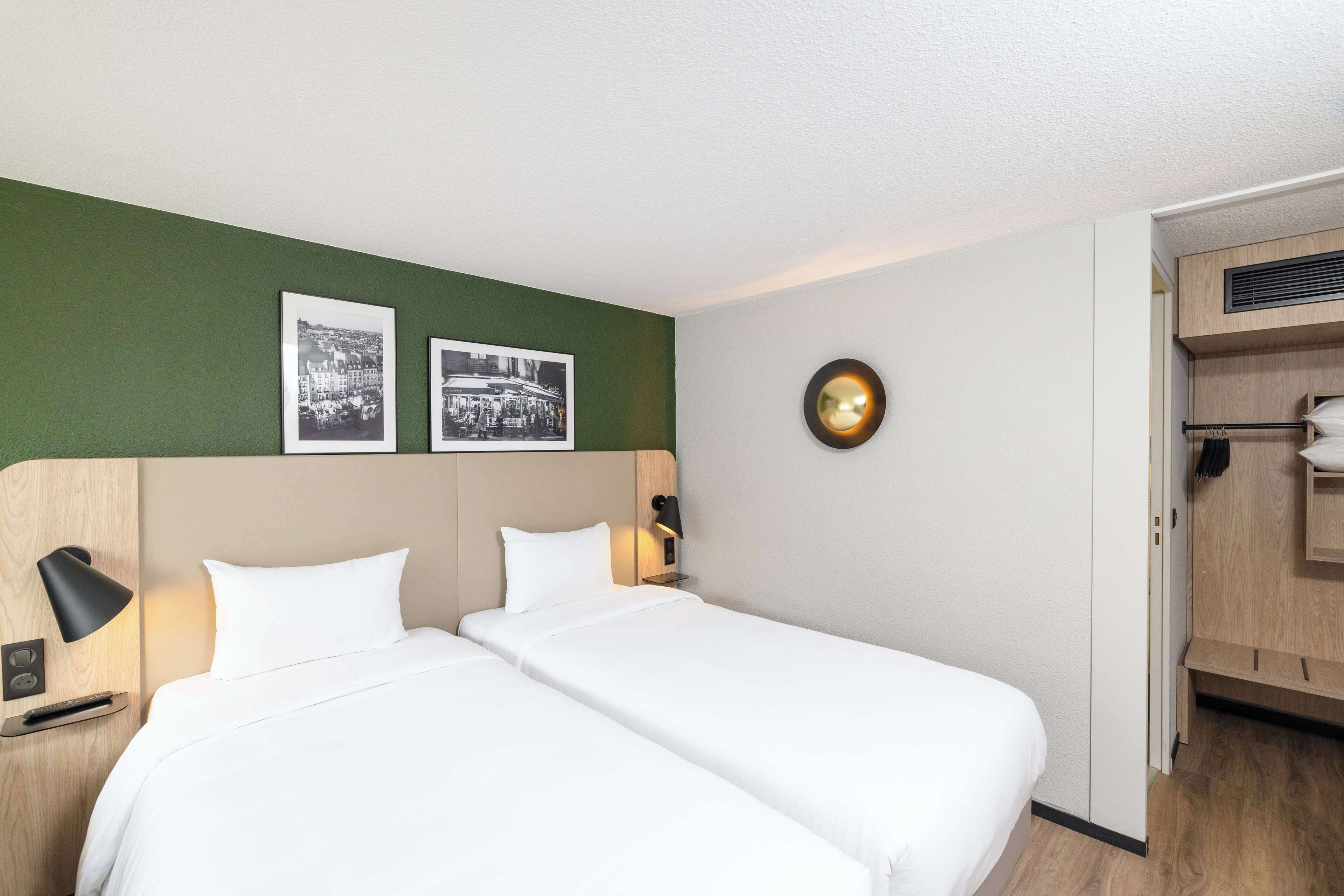 A hotel room with two beds, a green accent wall, and two black-and-white photographs.