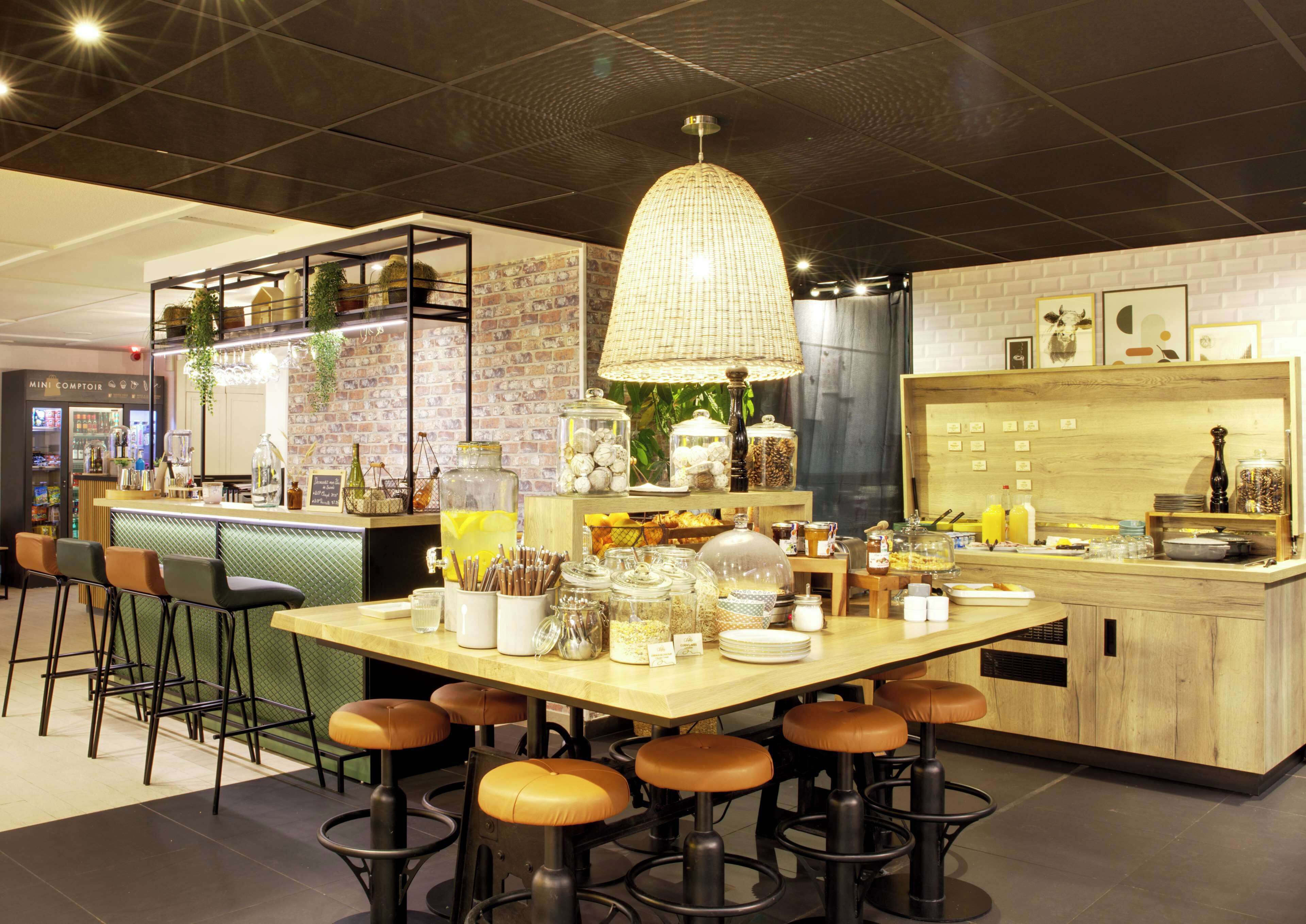 Un espace bar moderne avec des tabourets, un comptoir proposant divers plats et une suspension lumineuse.