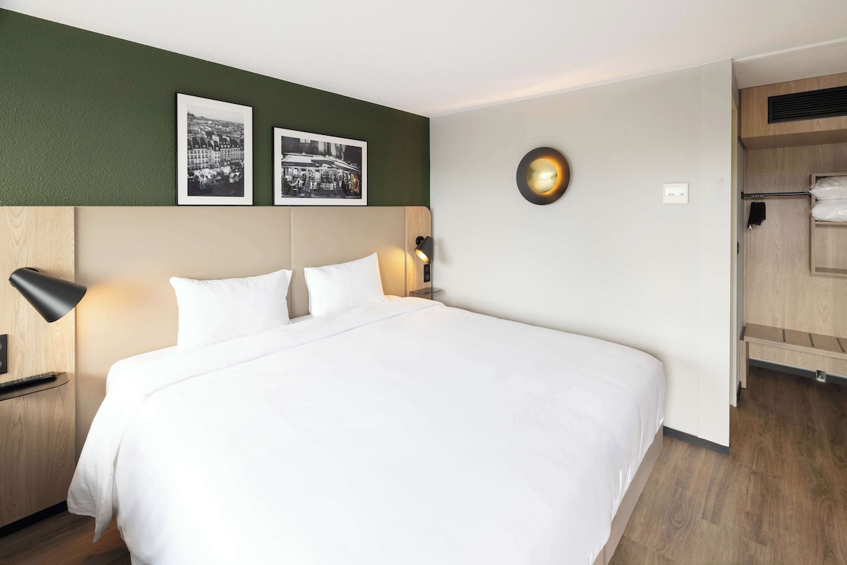 A neatly made bed with white linens, a bedside lamp, and two framed photographs on the wall above.