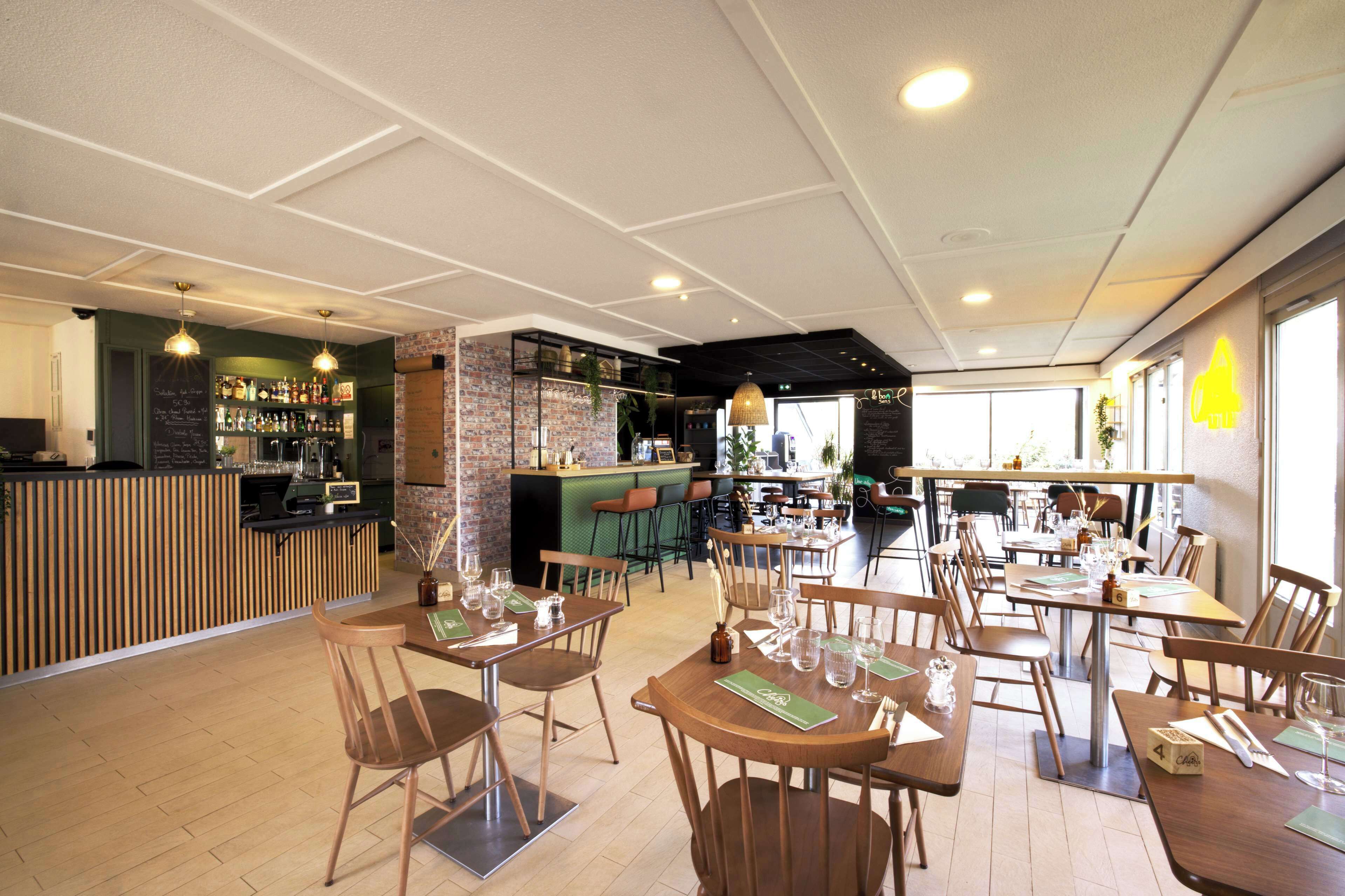 Un restaurante con mesas y sillas de madera, una zona de bar y vistas a la calle.