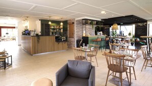 A modern bar area with wooden accents, a brick wall, and a seating area with wooden tables and chairs. - Campanile Nature - Taverny (Taverny)