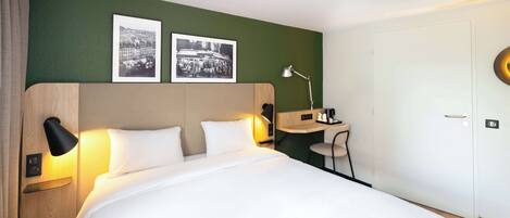 Habitación de hotel con una cama grande, dos lámparas de noche, un escritorio con una silla y dos cuadros en la pared.