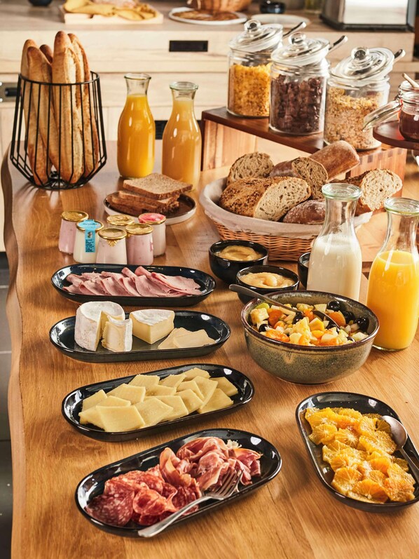 A breakfast buffet with various cheeses, meats, breads, and beverages.