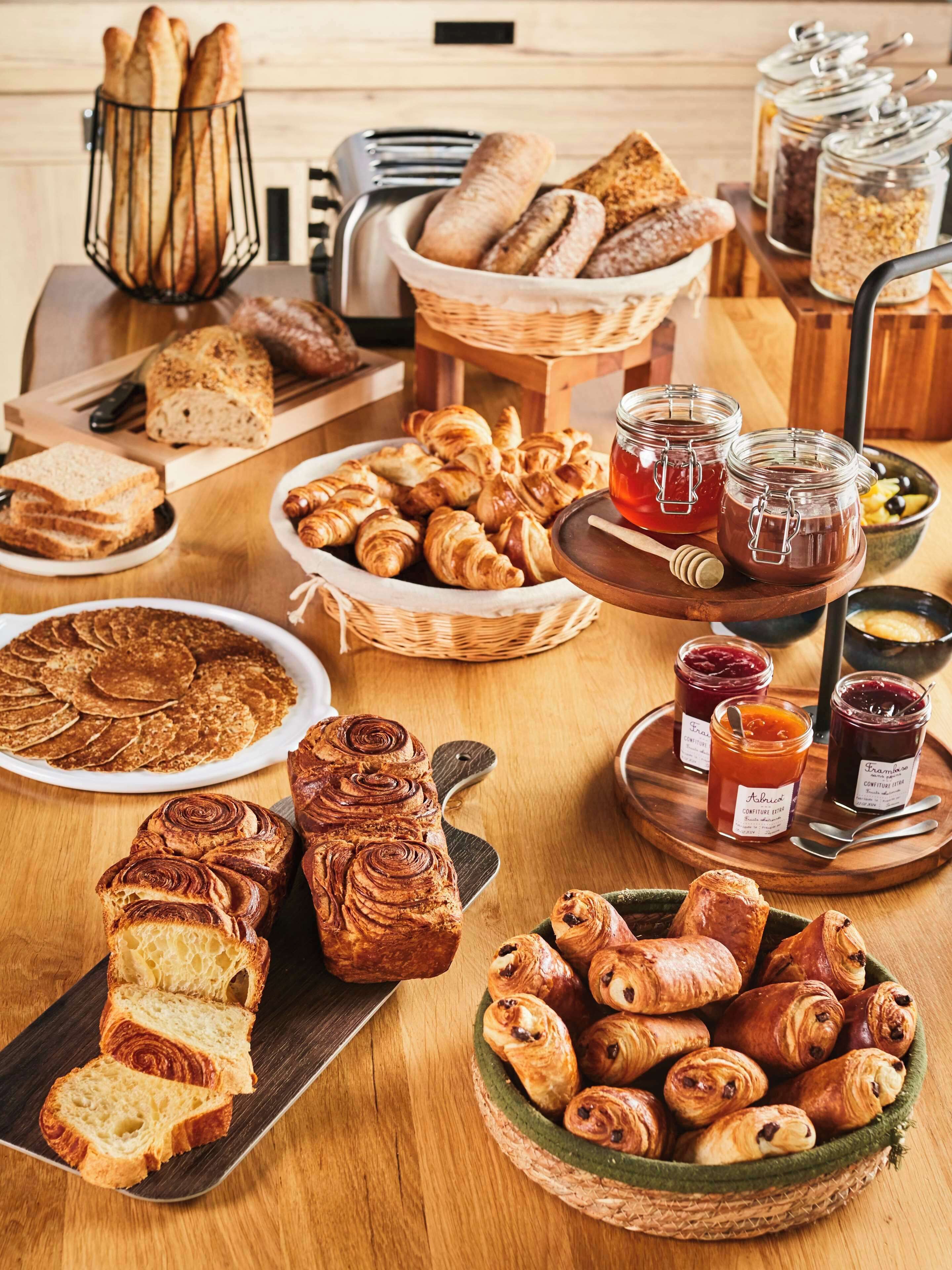 A variety of breads and pastries on a wooden table, including croissants, baguettes, and a loaf of bread.