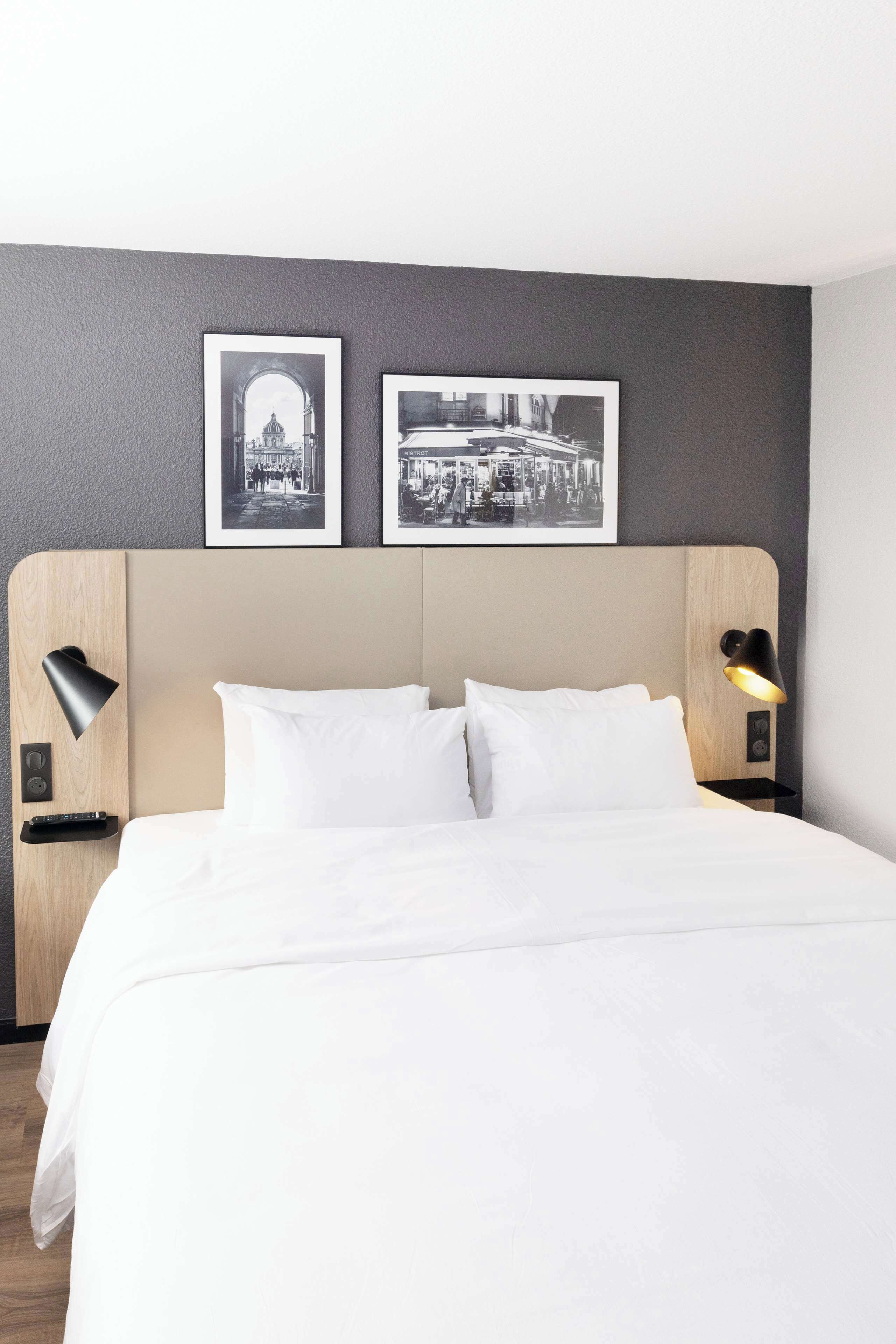 A hotel room with a large bed, two wall-mounted picture frames, and bedside lamps.