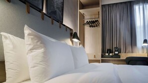 A neatly made bed with white linens, a bedside table with a lamp, and a wooden headboard. - Campanile Nature - Taverny (Taverny)