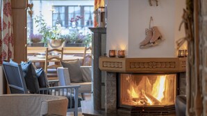 A cozy living room with a stone fireplace, a sofa, and a dining area with a view of the outdoors. - Hotel Chesa Valese (Zermatt)