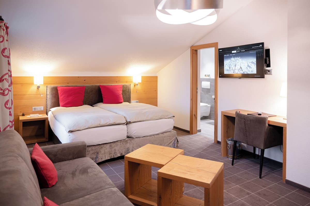 A modern hotel room with a bed, a sofa, a desk, and a TV.