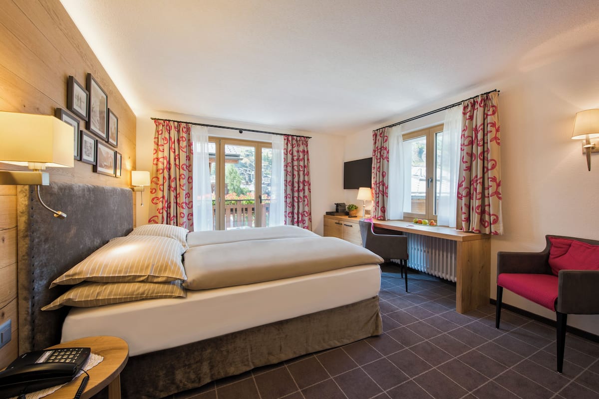 A hotel room with a bed, desk, chair, and a view of the outdoors.