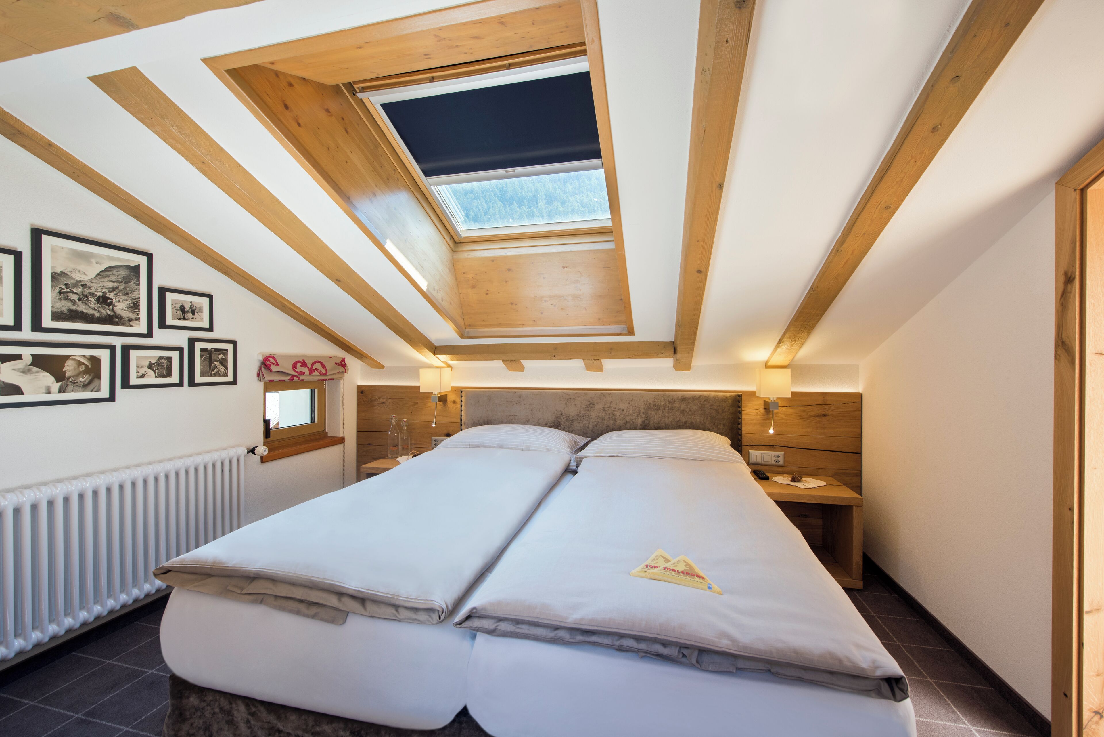 Une chambre avec une lucarne, un lit avec deux oreillers, une table de chevet avec une lampe et des tableaux encadrés au mur.