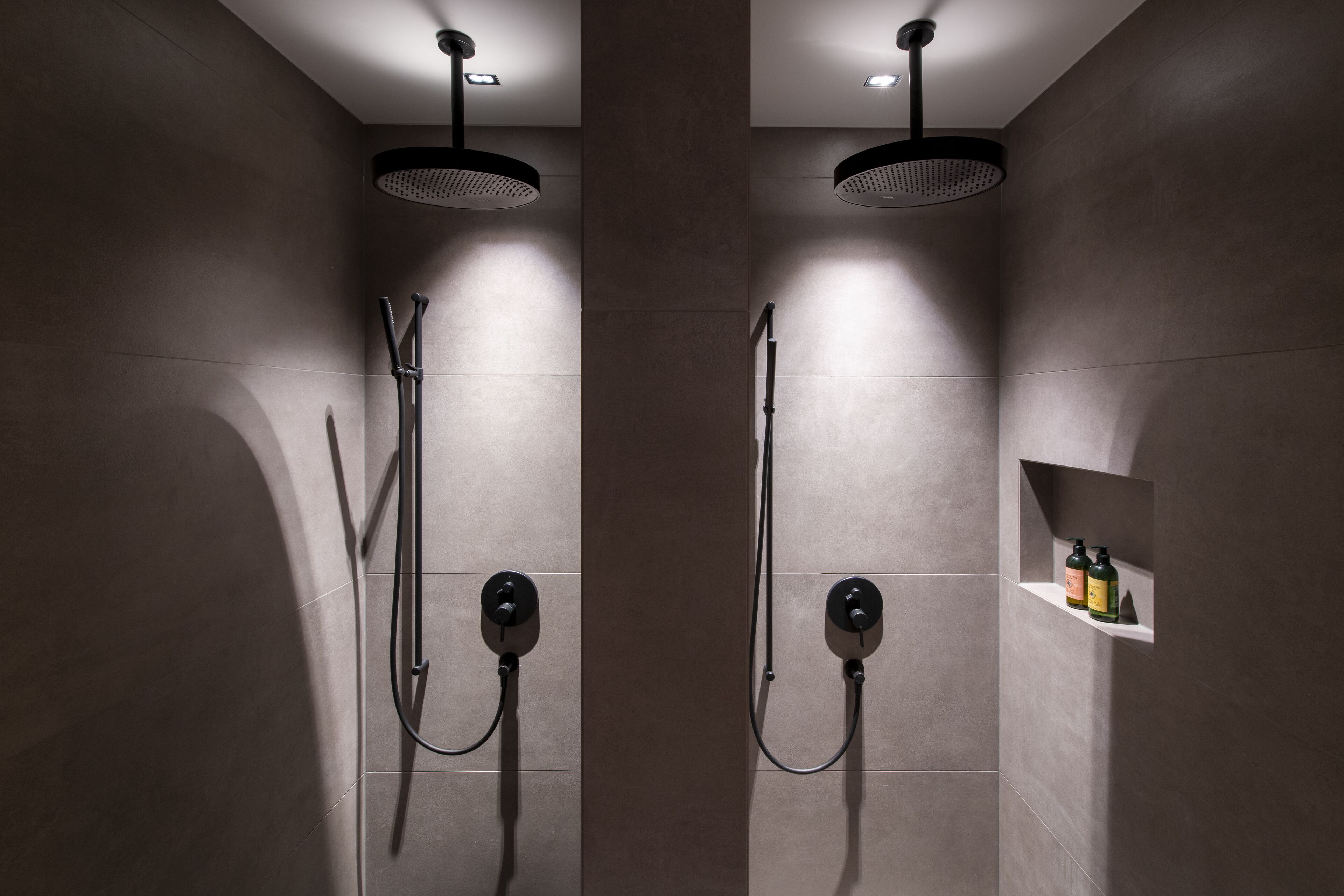 Un espace douche moderne doté de deux pommes de douche et d’une étagère pour les articles de toilette.