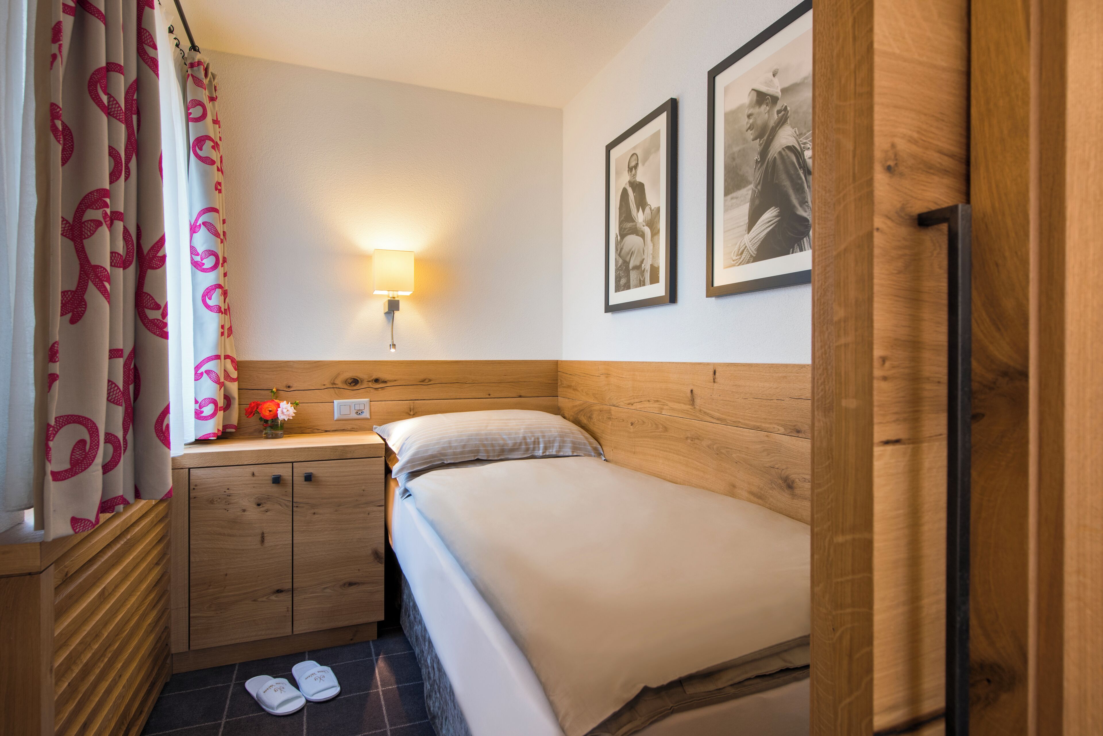 Une petite chambre à coucher, bien rangée, avec un lit simple, une table de chevet, une lampe et un tableau encadré au mur.