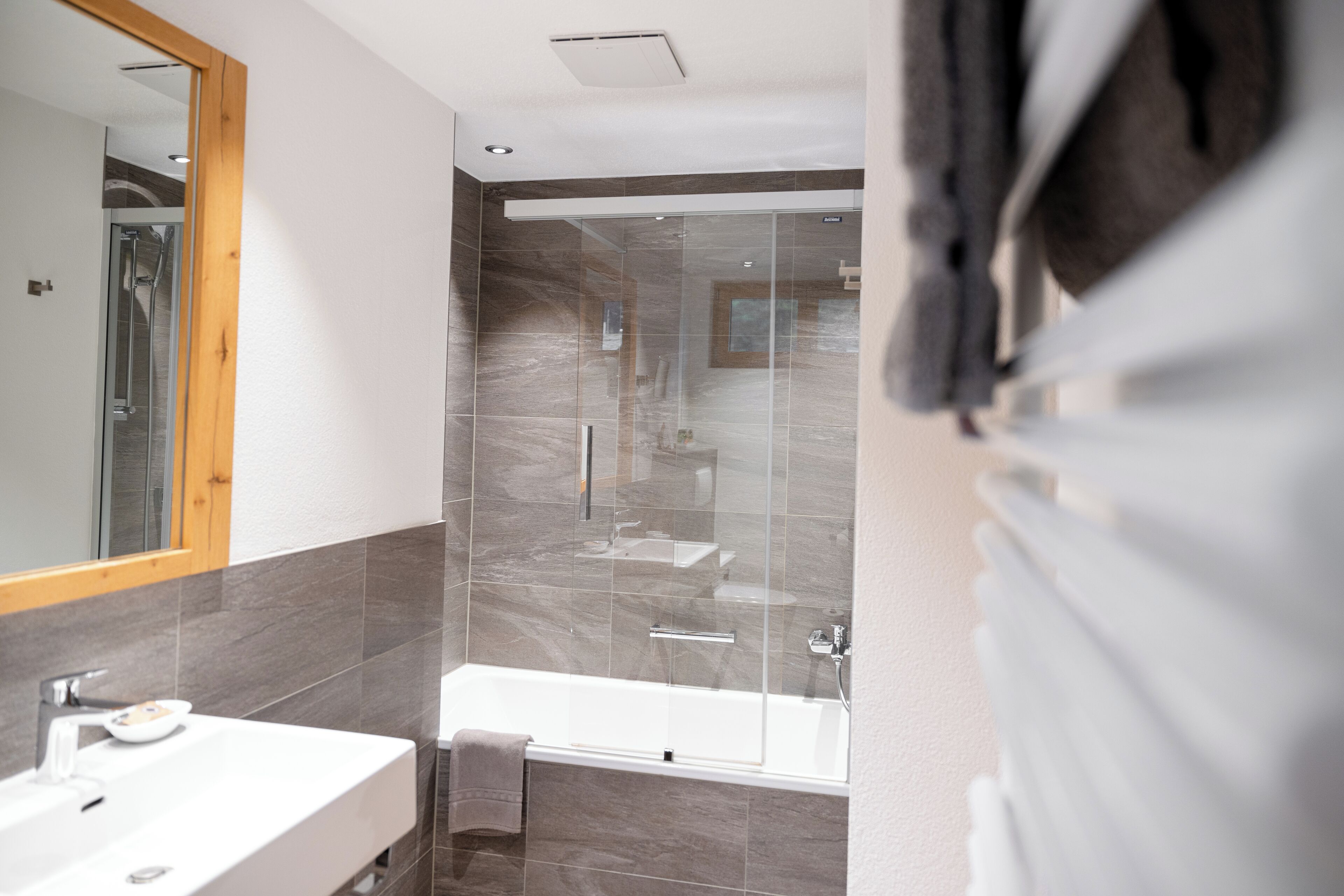A modern bathroom with a glass shower enclosure, a bathtub, and a vanity with a mirror.