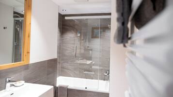 A modern bathroom with a glass shower enclosure, a bathtub, and a vanity with a mirror.