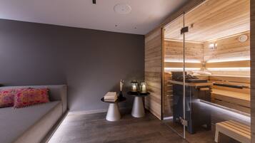 A modern room with a sofa, two side tables, a wooden bench, and a sauna area with a glass door.