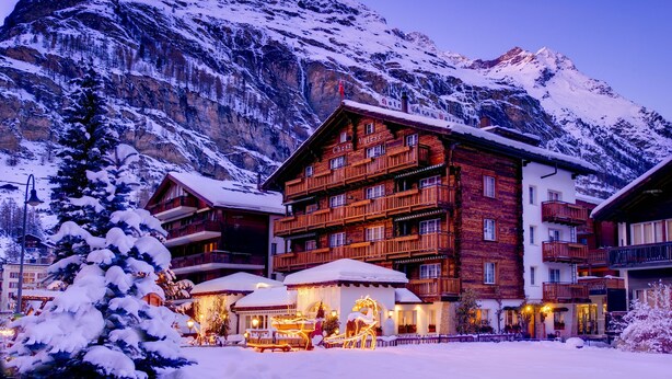 A multi-story wooden building with balconies, surrounded by snow-covered mountains. - Hotel Chesa Valese (Zermatt)