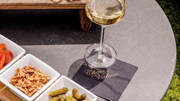 Un tavolo rotondo con un tagliere di formaggi, un bicchiere di vino bianco e ciotoline con stuzzichini.