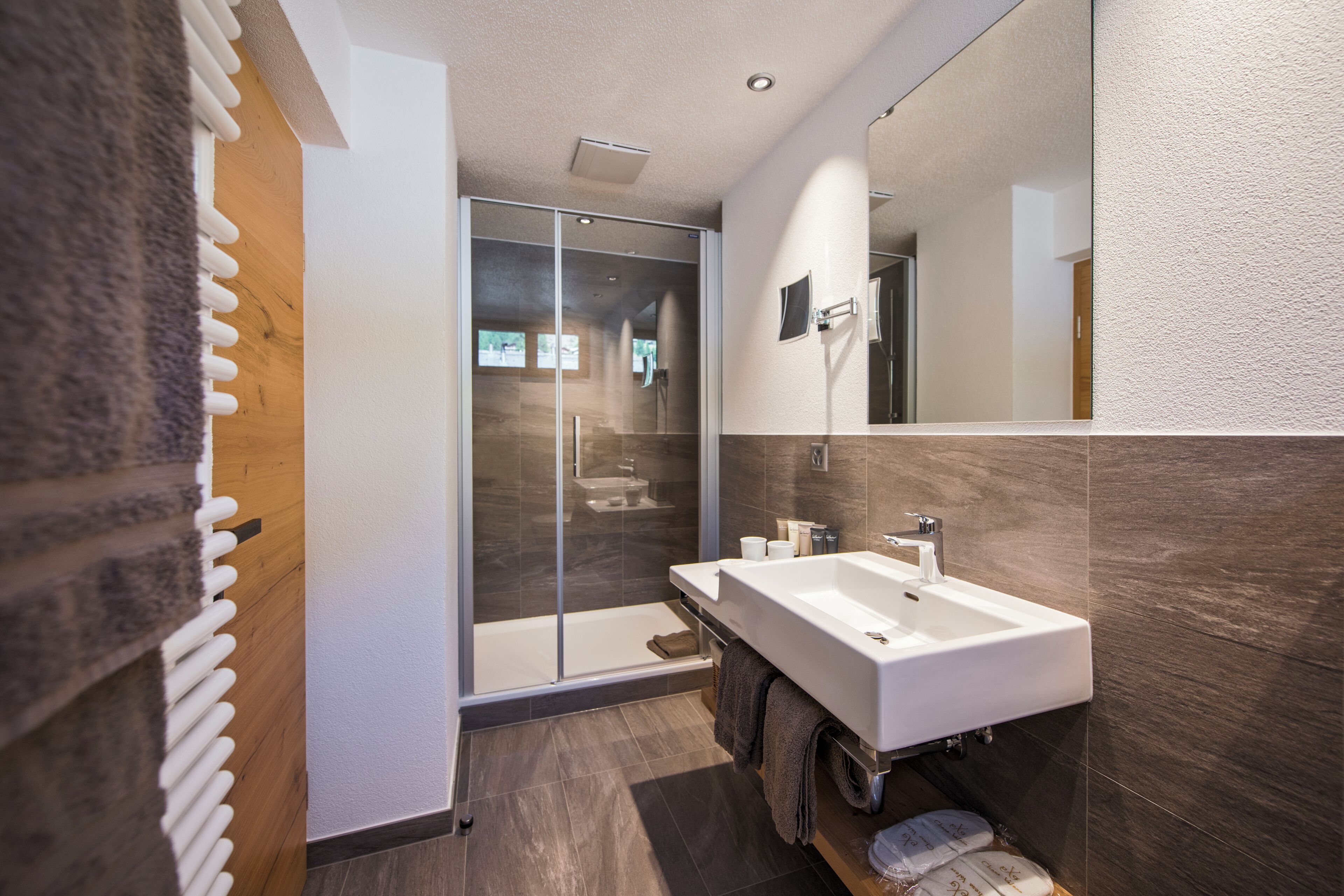 A modern bathroom with a large mirror, a double sink, and a glass-enclosed shower.