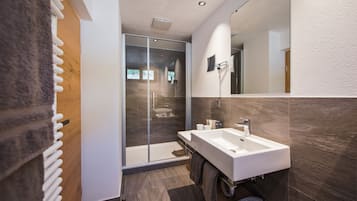 A modern bathroom with a large mirror, a double sink, and a glass-enclosed shower.