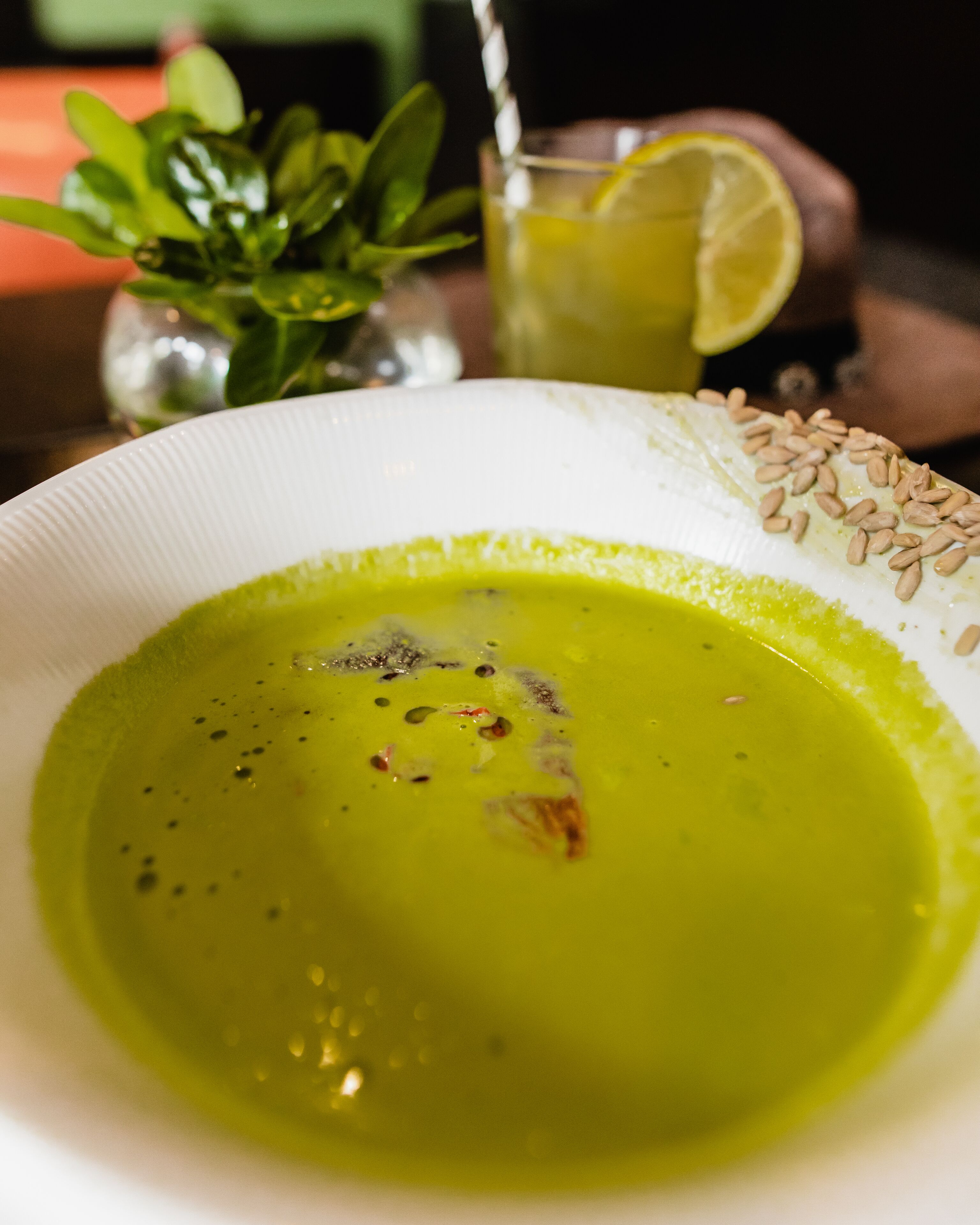 A bowl of green soup with a lemon slice and seeds on the side.