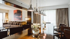 Un vestíbulo de hotel con un mostrador de recepción de madera, un sofá y sillas. Hay lámparas colgantes y un cuadro grande en la pared.