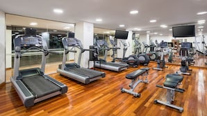 Un gimnasio con varias cintas de correr, elípticas y bancos de pesas.