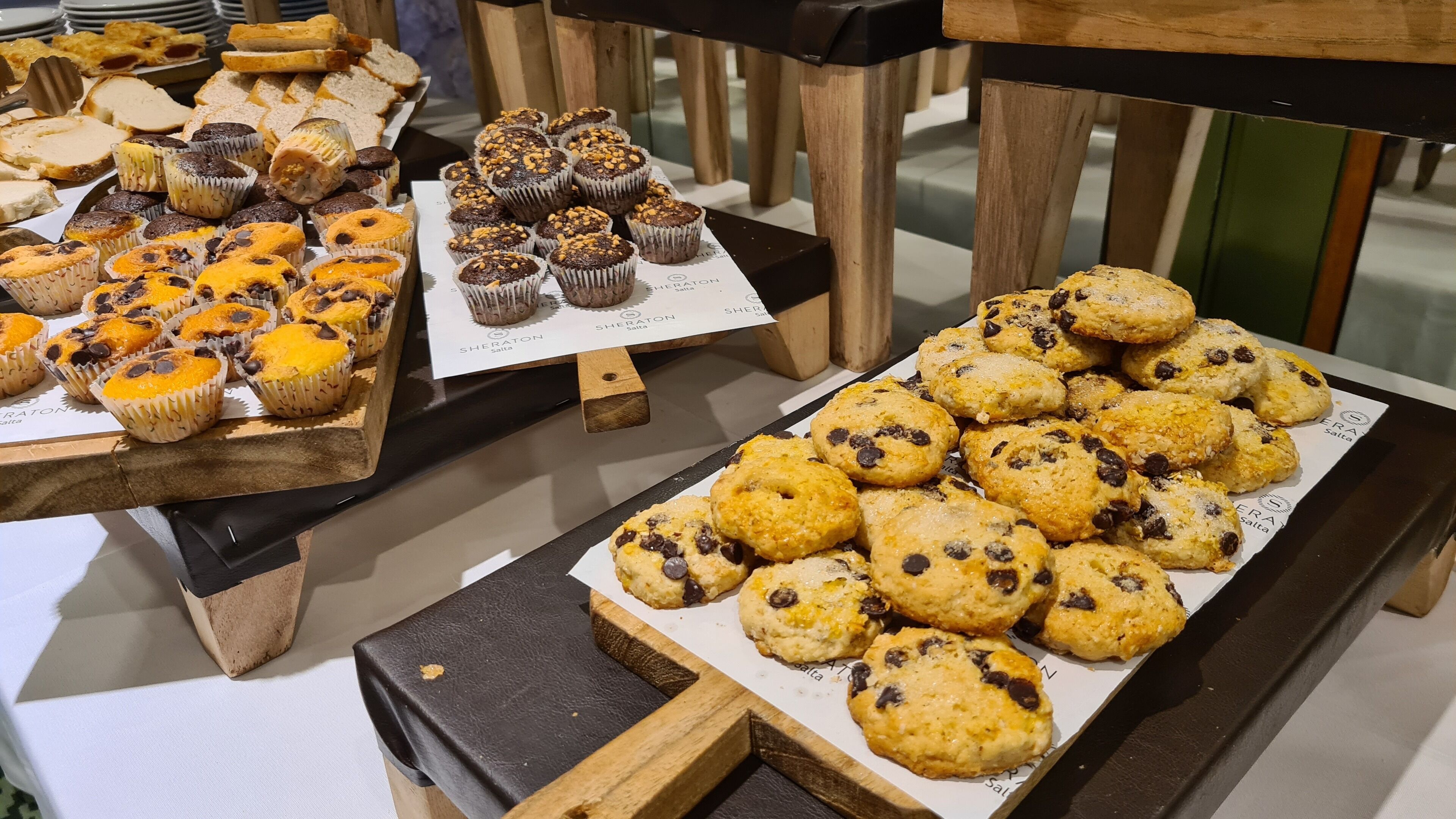 A display of various baked goods including muffins and cookies on wooden serving boards.
