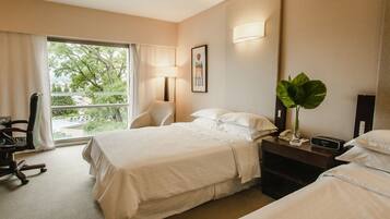 Una habitación de hotel con una cama, una silla, un escritorio con lámpara, teléfono y una planta.