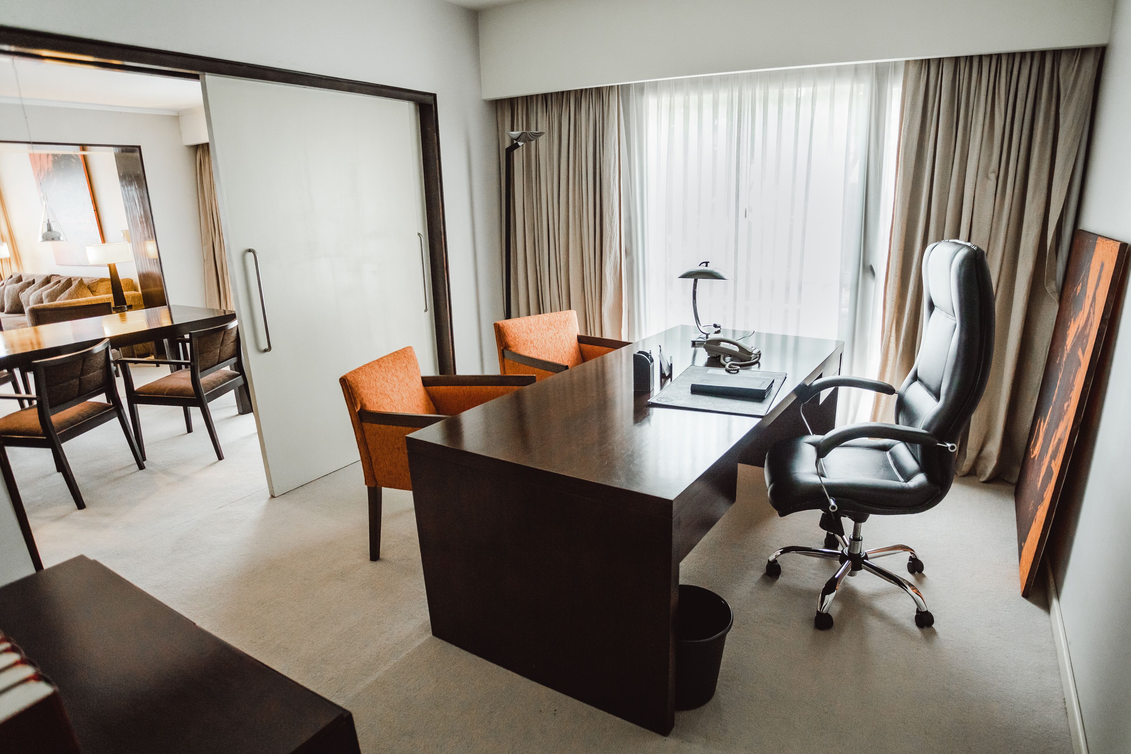 A hotel room with a large desk, two chairs, a laptop, and a desk lamp.