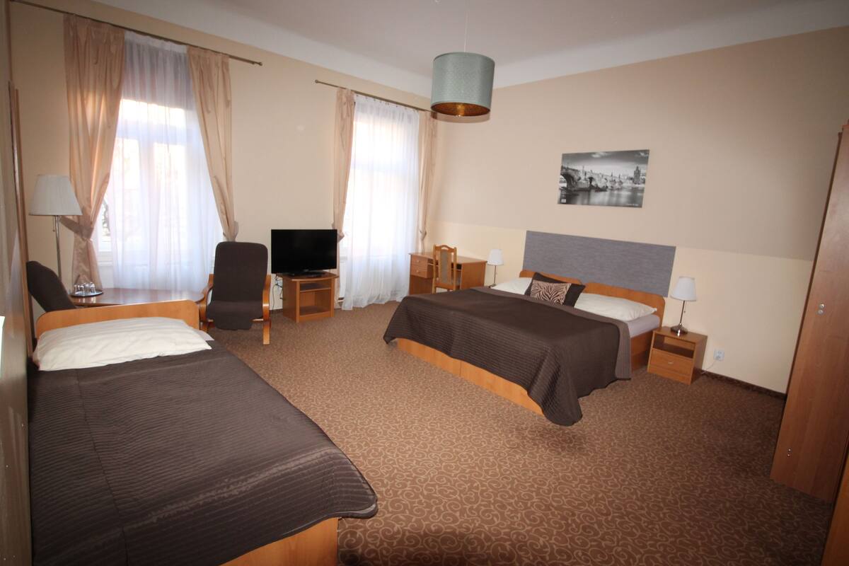 A hotel room with two beds, a desk, a chair, a TV, and a lamp.