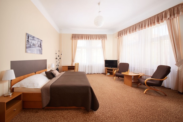 A hotel room with a bed, a desk, a chair, a television, and a painting on the wall. - Hotel City Bell (Prague)