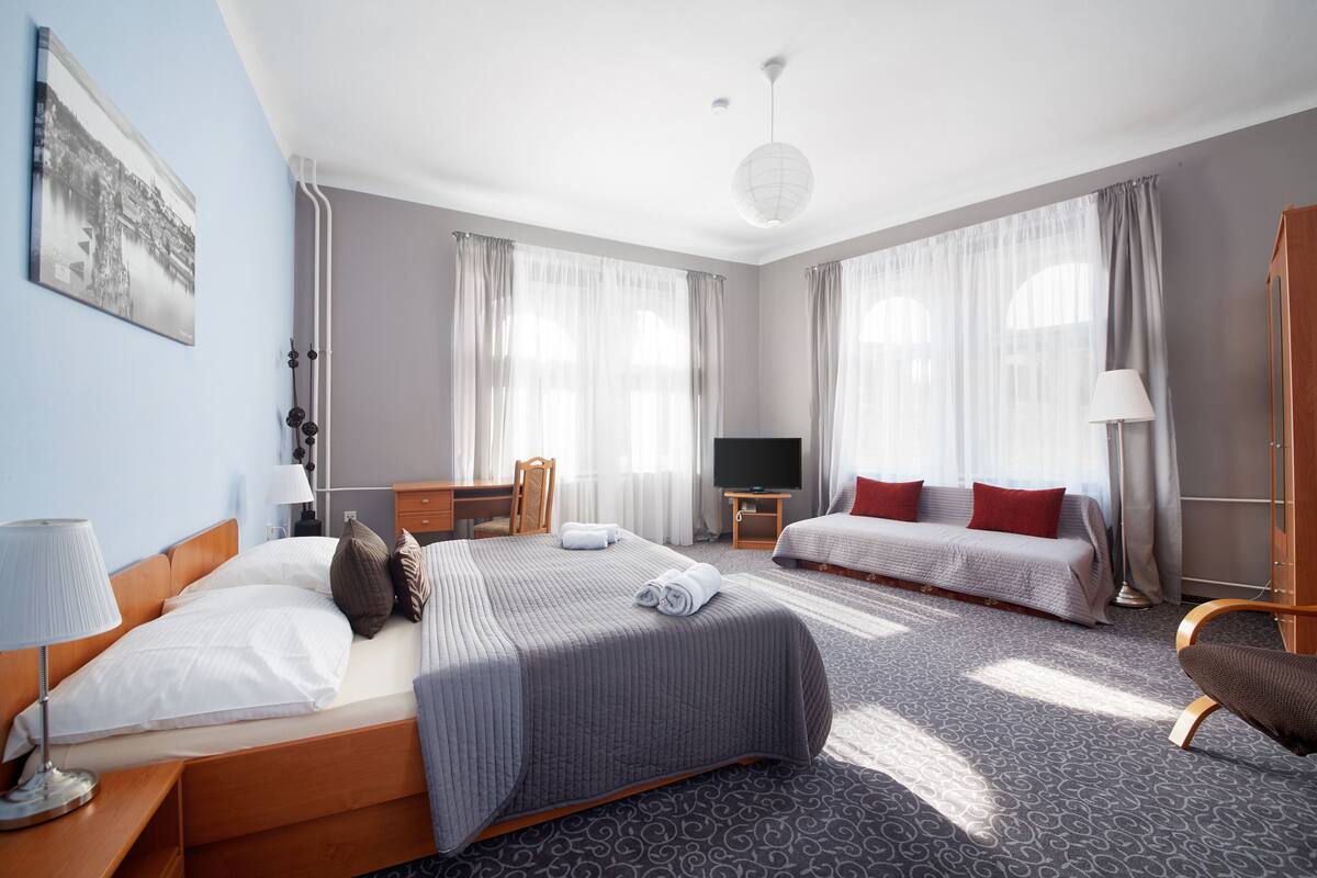 A hotel room with a bed, a desk, a TV, a sofa, and a chair.