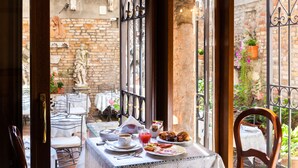 Ein Tisch gedeckt mit Frühstücksangeboten, eine Statue und Blick auf eine Ziegelwand und einen Garten.